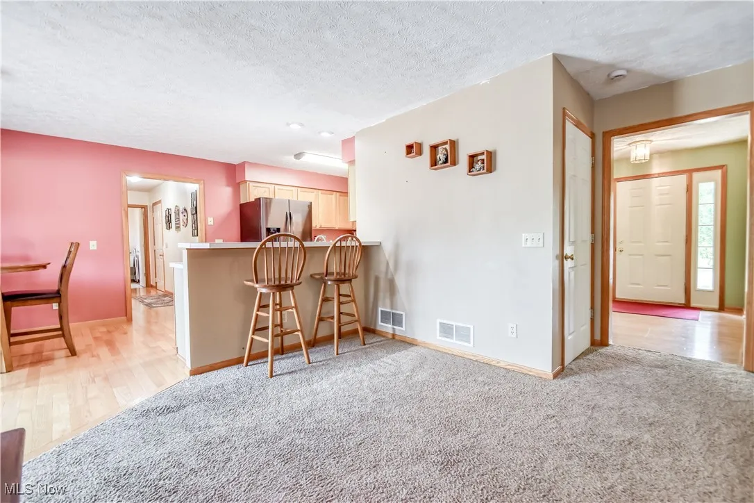 Kitchen featuring a breakfast bar area, a textured ceiling, stainless steel fridge with ice dispenser, light countertops, and light colored carpet
