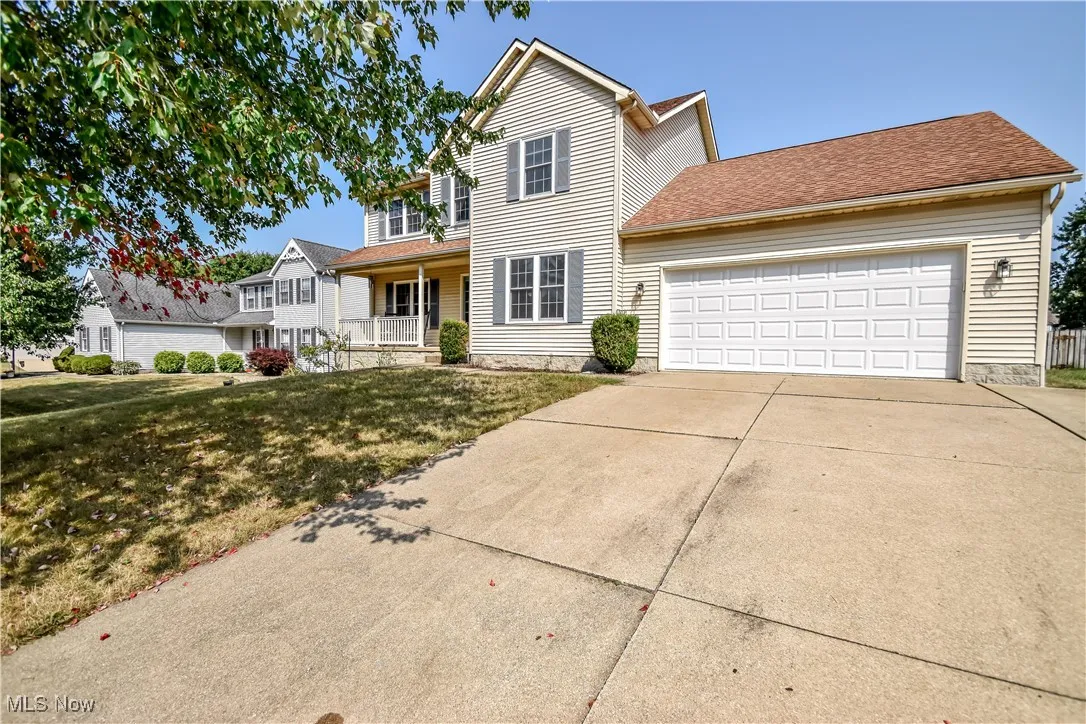 Traditional home featuring covered porch, a shingled roof, driveway, a garage, and a front yard