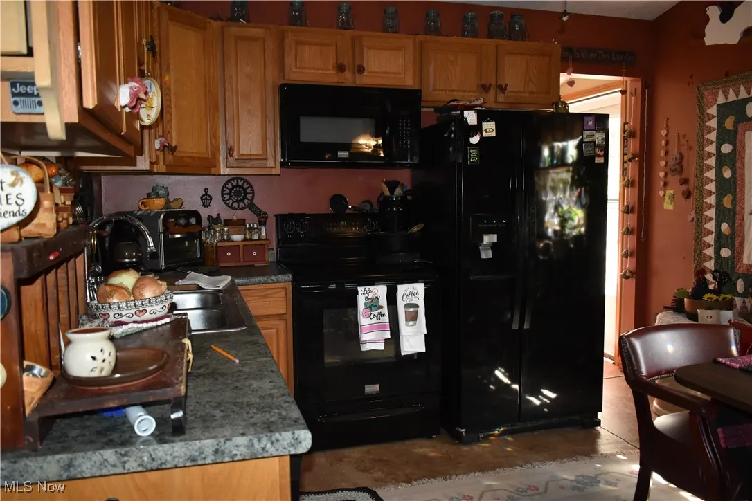 Kitchen featuring black appliances, dark countertops, and brown cabinets