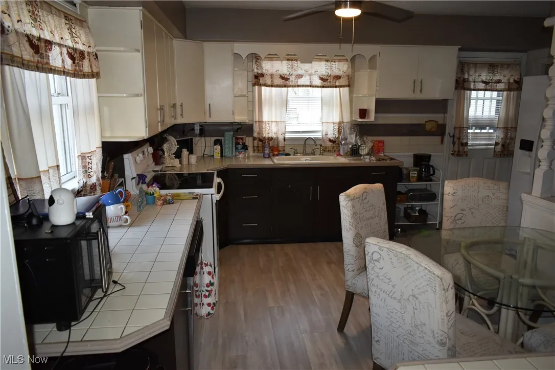 Kitchen with tile countertops, open shelves, white cabinetry, black microwave, and dark cabinets