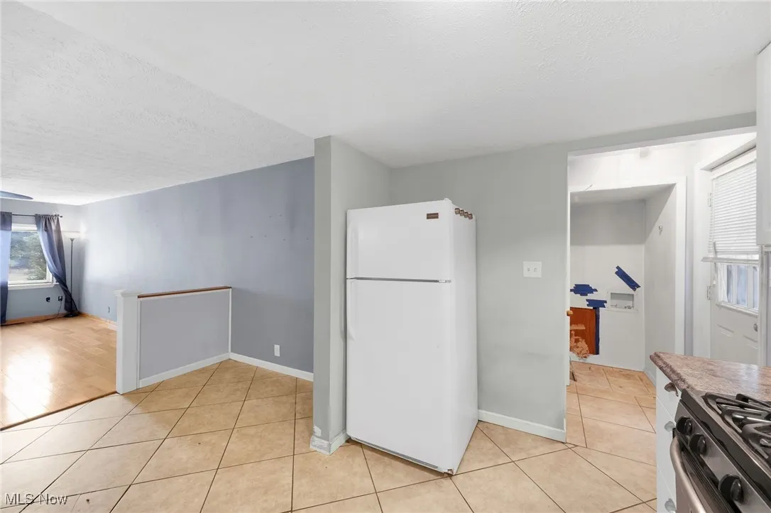 Kitchen with healthy amount of natural light, freestanding refrigerator, a textured ceiling, stainless steel range with gas stovetop, and light tile patterned floors