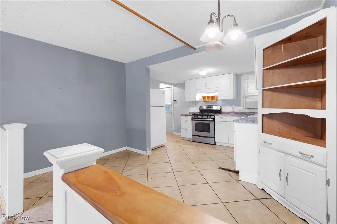 Kitchen with white cabinets, stainless steel range with gas cooktop, light tile patterned floors, pendant lighting, and open shelves