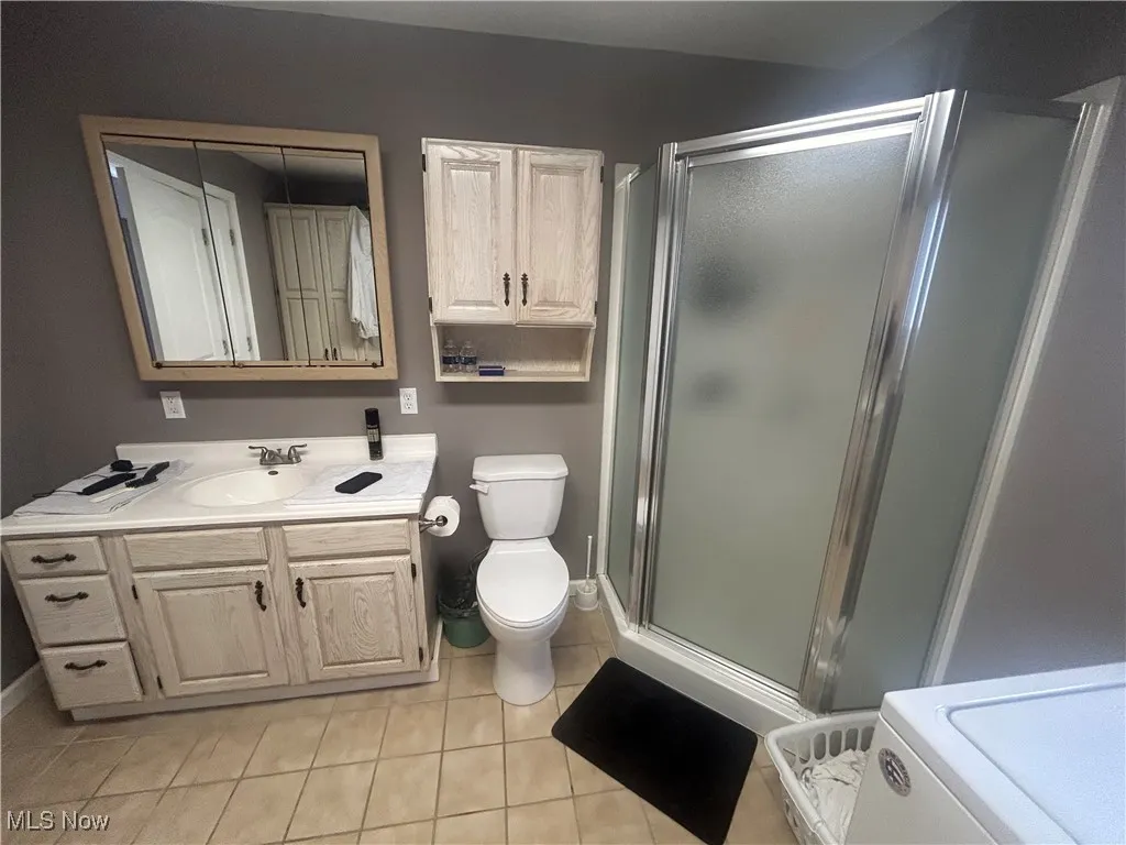 Full bath featuring a stall shower, vanity, light tile patterned flooring, and washer / dryer