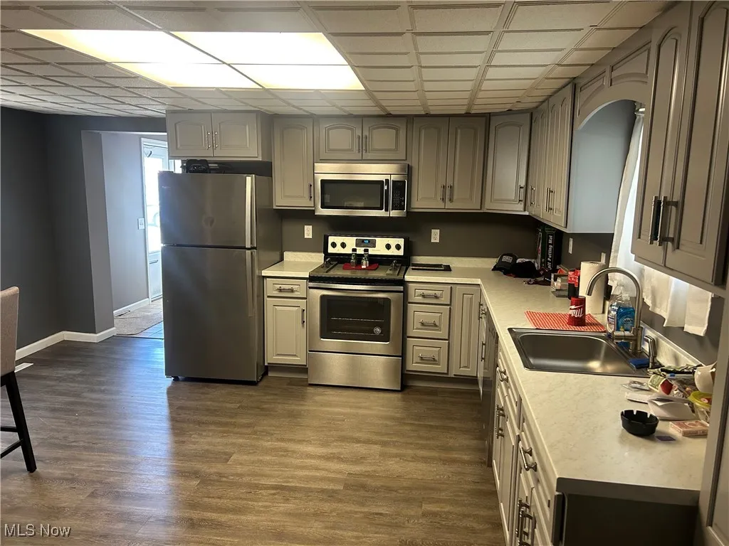 Kitchen featuring appliances with stainless steel finishes, light countertops, dark wood-type flooring, a paneled ceiling, and gray cabinets