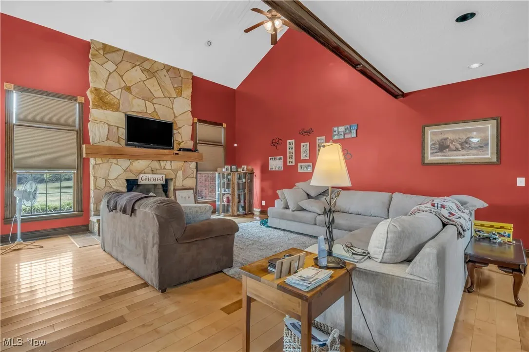 Living room with hardwood / wood-style flooring, high vaulted ceiling, a stone fireplace, and ceiling fan