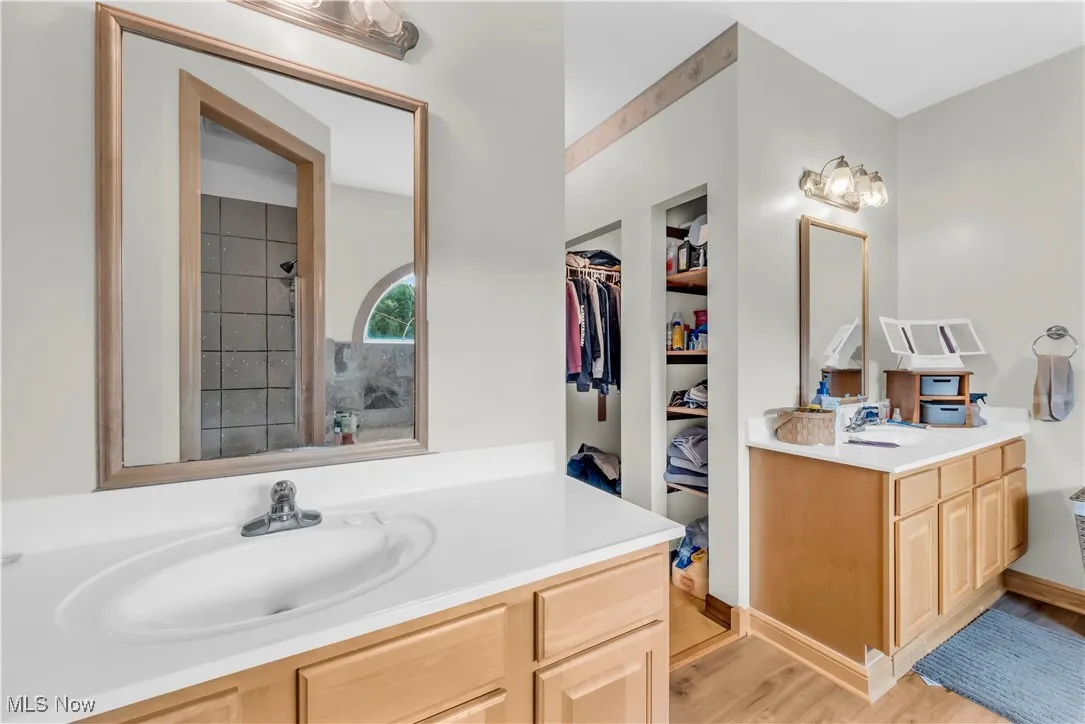 Bathroom with twin his and hers vanities, light wood-type flooring, dual walk in closets and a shower