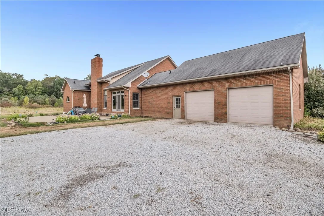 View of front of home with brick siding, an attached garage, driveway, a chimney, and a patio area