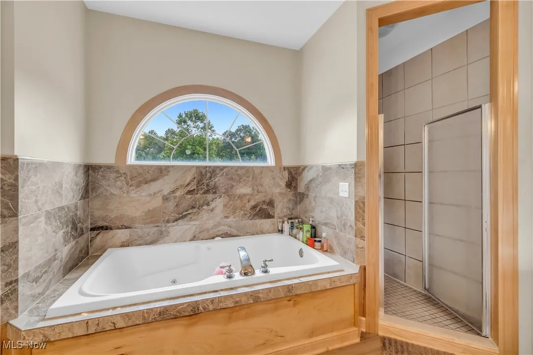 Full bath featuring a whirlpool tub, walk in shower, and tile walls