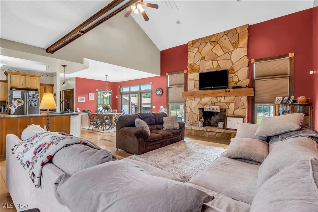 Living area with high vaulted ceiling, a fireplace, a ceiling fan, light wood-style flooring, and beamed ceiling