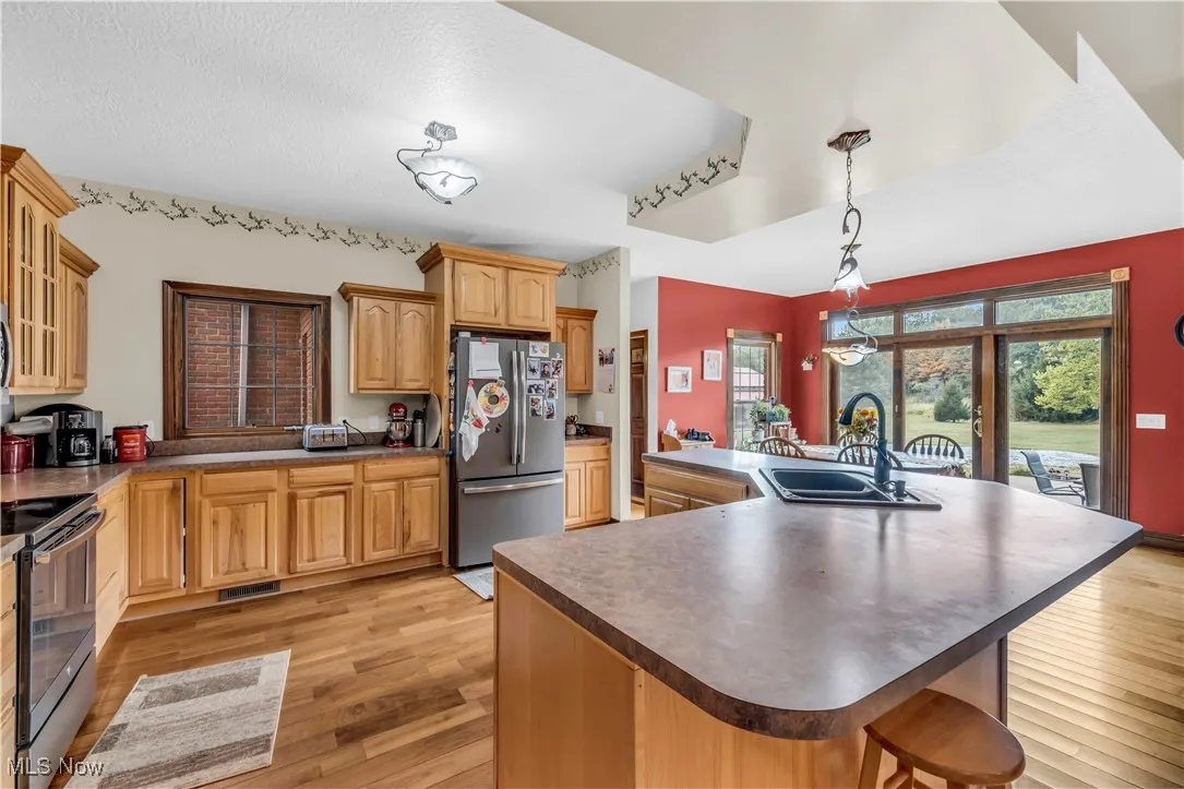 Kitchen featuring stainless steel appliances, a kitchen island with sink, light wood-type flooring, dark countertops, and a breakfast bar