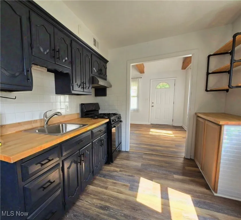 Kitchen featuring butcher block counters, black range with gas cooktop, dark wood finished floors, under cabinet range hood, and open shelves