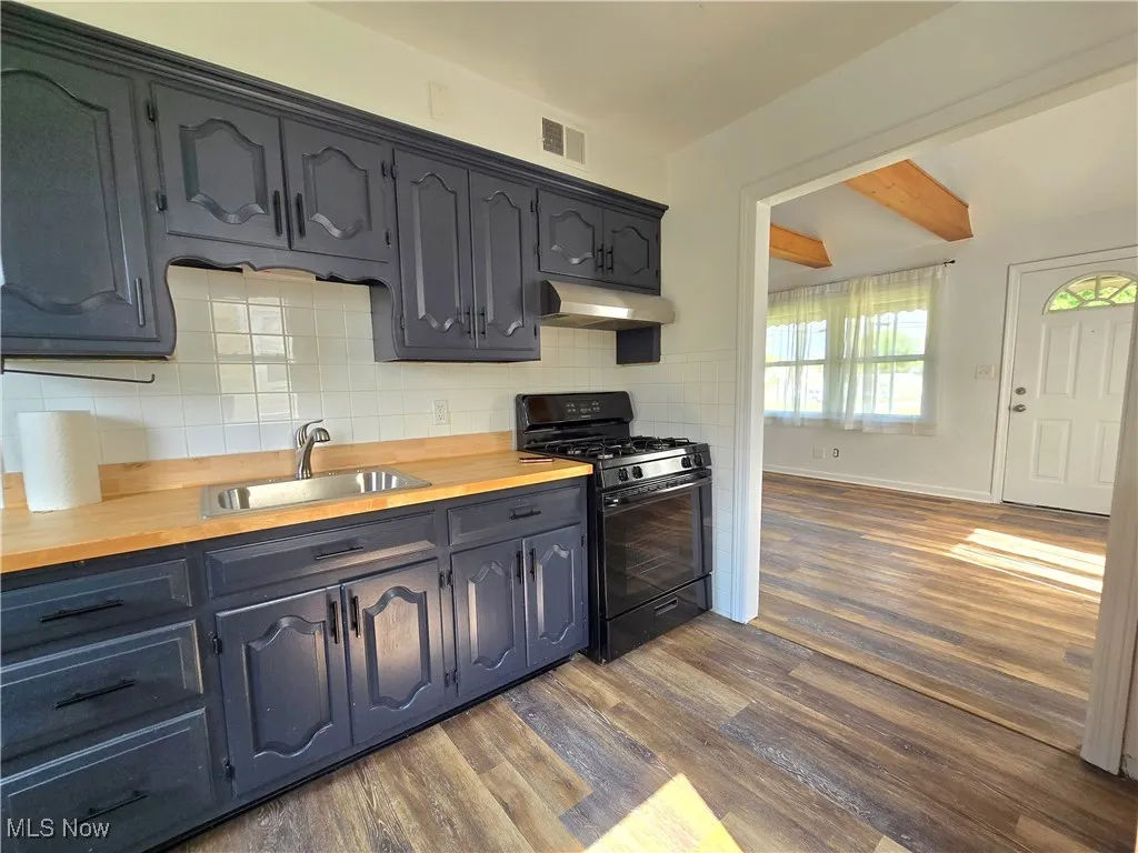 Kitchen featuring black gas range, dark wood-type flooring, under cabinet range hood, decorative backsplash, and wooden counters