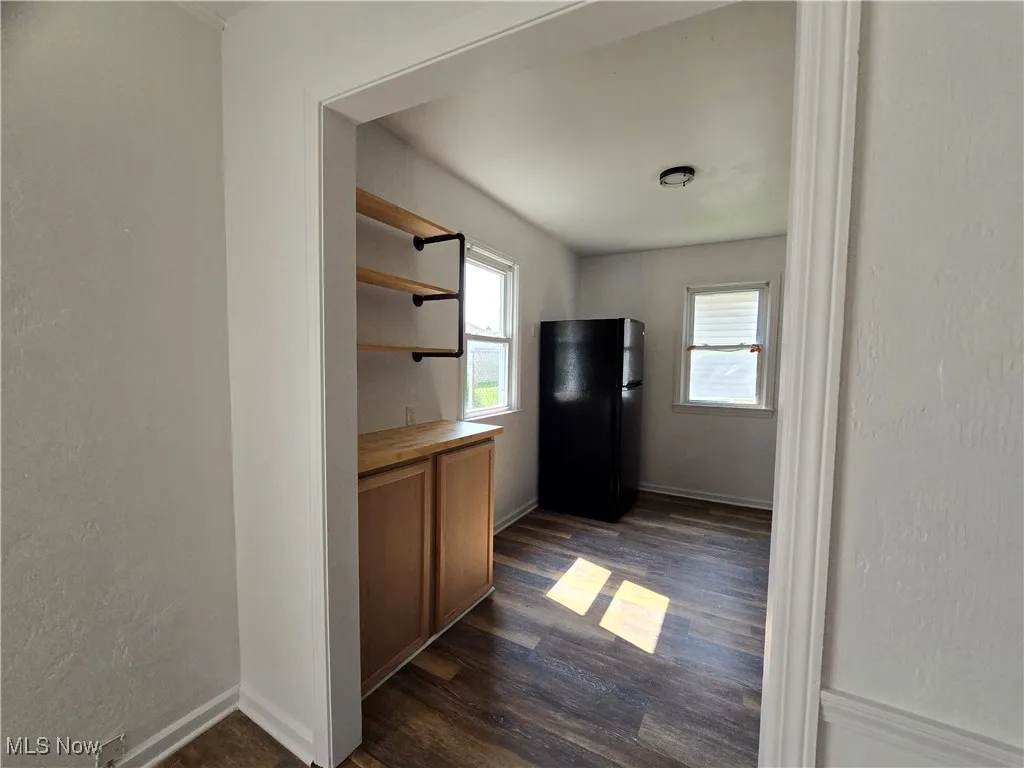 Kitchen with open shelves, a textured wall, freestanding refrigerator, dark wood-style flooring, and brown cabinets