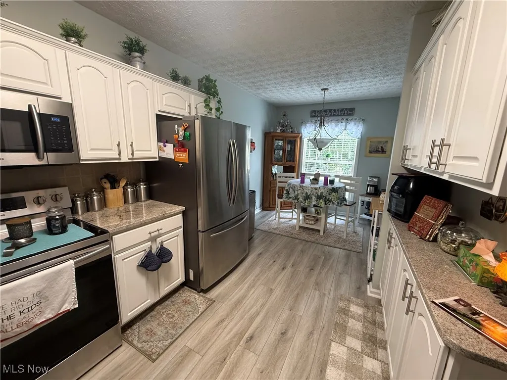 Kitchen with appliances with stainless steel finishes, a textured ceiling, pendant lighting, light wood-type flooring, and tasteful backsplash