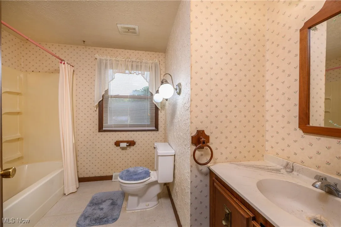 Full bath with shower / bath combination with curtain, vanity, wallpapered walls, light tile patterned floors, and a textured ceiling