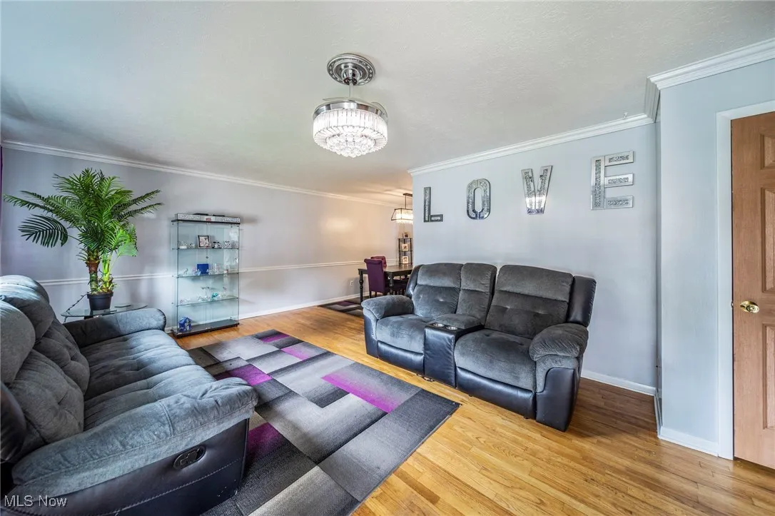 Living area with ornamental molding, wood finished floors, and a chandelier