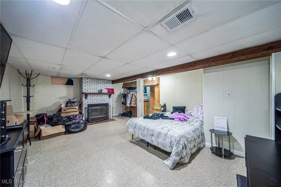 Bedroom with a fireplace, a drop ceiling, wooden walls, light floors, and recessed lighting