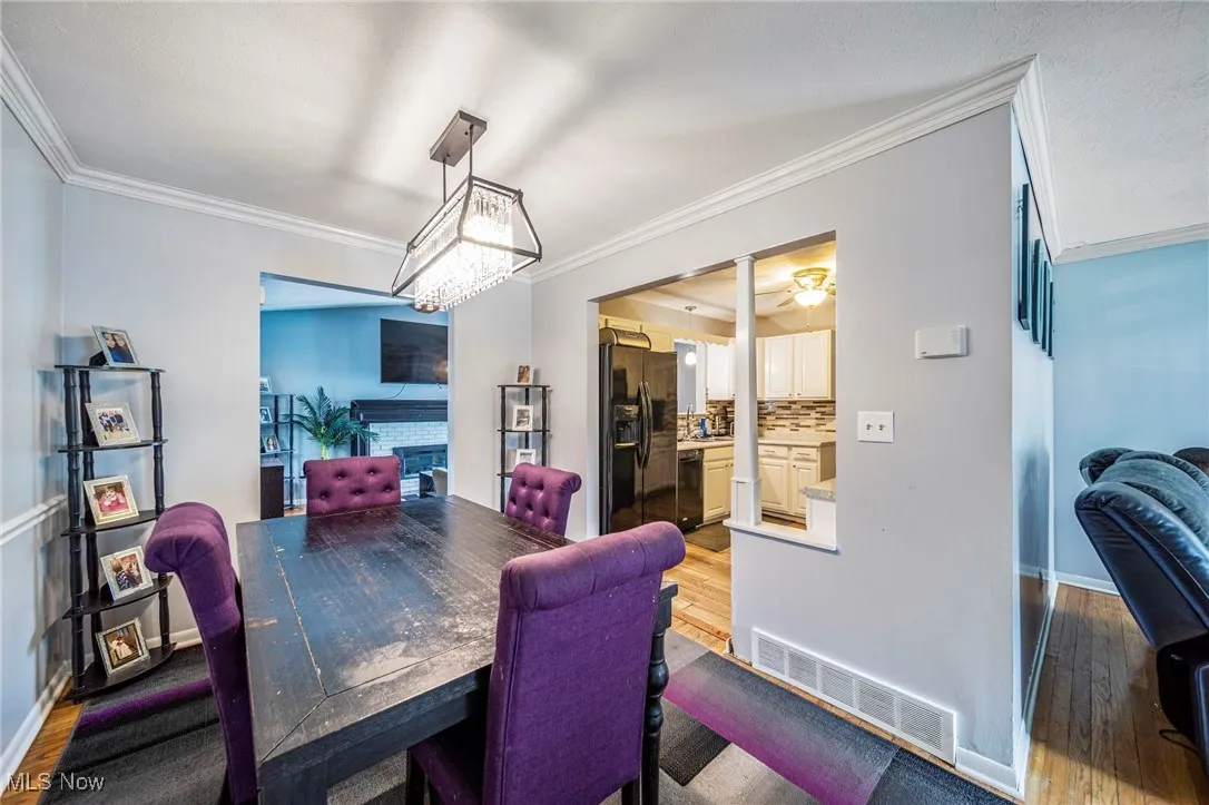Dining room with crown molding, light wood-style flooring, a fireplace, a chandelier, and a ceiling fan