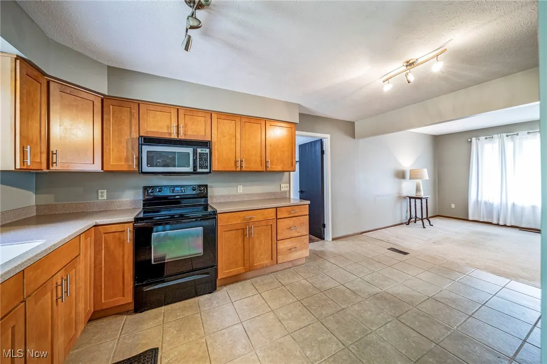 Kitchen with brown cabinets, black range with electric stovetop, rail lighting, and a textured ceiling