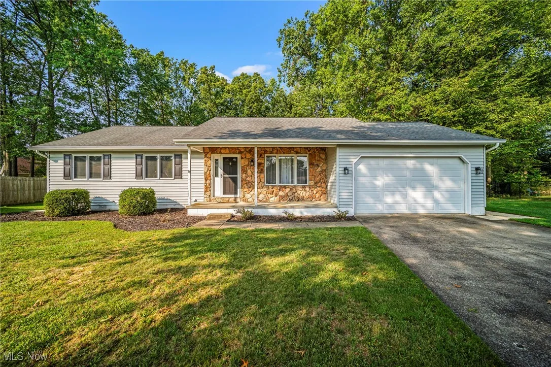 Single story home with covered porch, driveway, a garage, a shingled roof, and stone siding