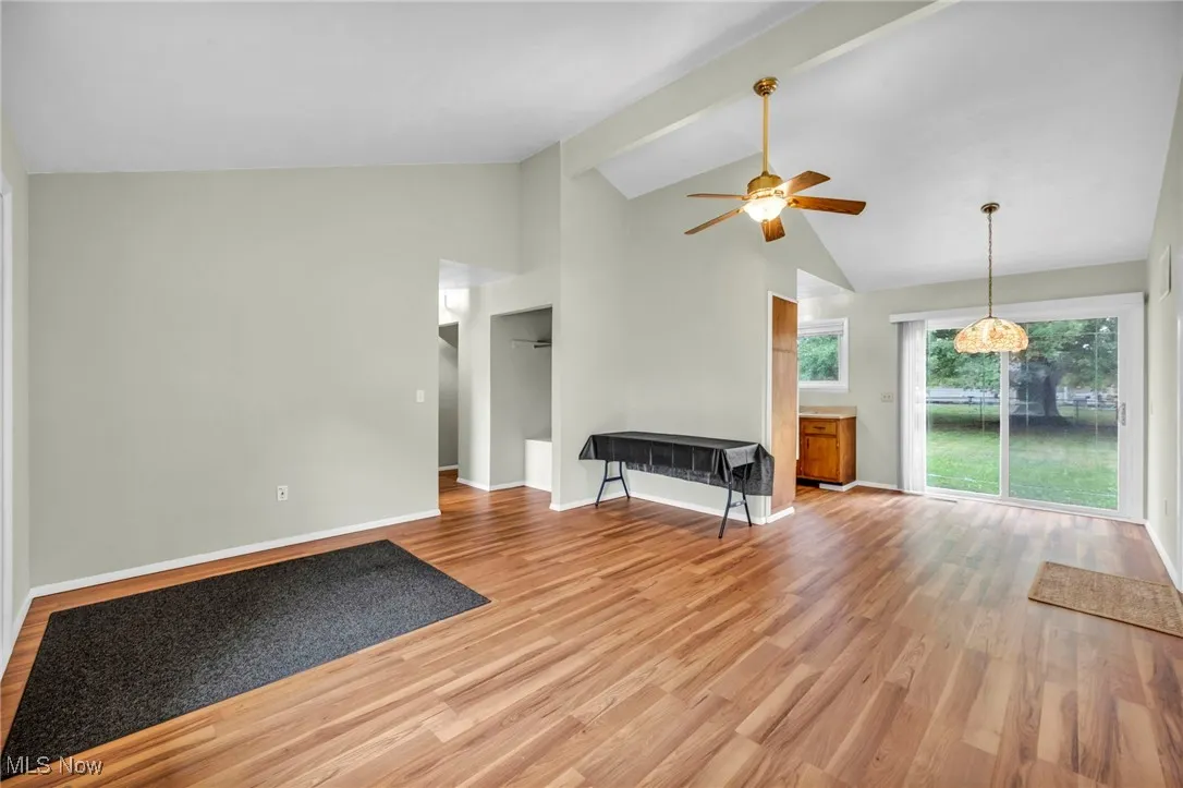 Unfurnished living room with high vaulted ceiling, light wood-type flooring, beam ceiling, and a ceiling fan