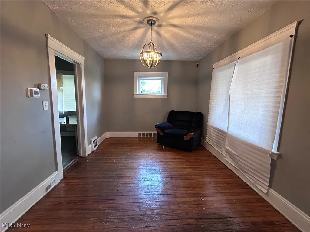Unfurnished room with dark wood-type flooring, a textured ceiling, and a chandelier