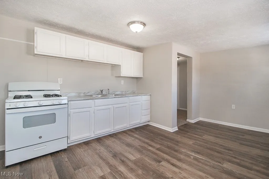 Kitchen featuring white range with gas stovetop, white cabinetry, light countertops, a textured ceiling, and dark wood finished floors