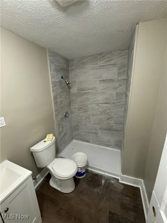 Bathroom with a textured ceiling, wood finished floors, a shower stall, and vanity