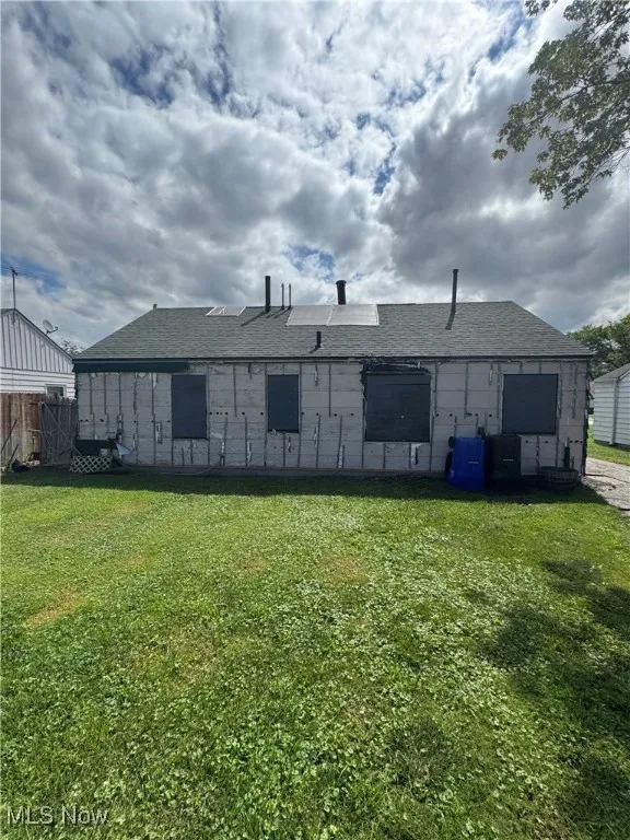 Rear view of property with a shingled roof and a yard
