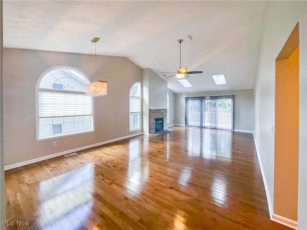 Unfurnished living room with ceiling fan, a stone fireplace, light wood-style floors, lofted ceiling, and a chandelier