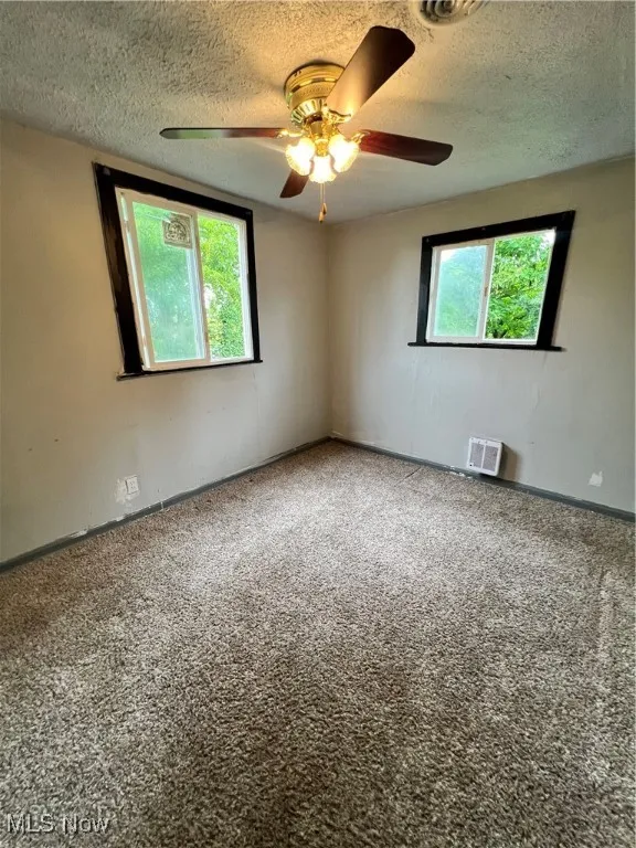 Carpeted empty room featuring a textured ceiling and a ceiling fan