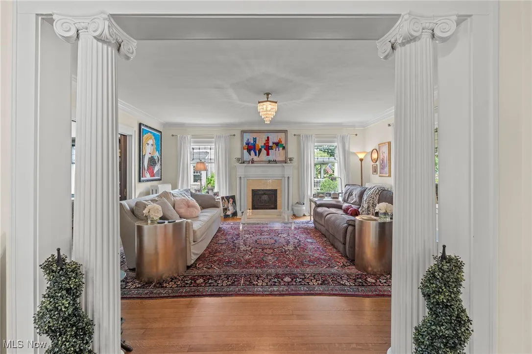 Living area featuring ornate columns, wood finished floors, ornamental molding, and a fireplace with raised hearth