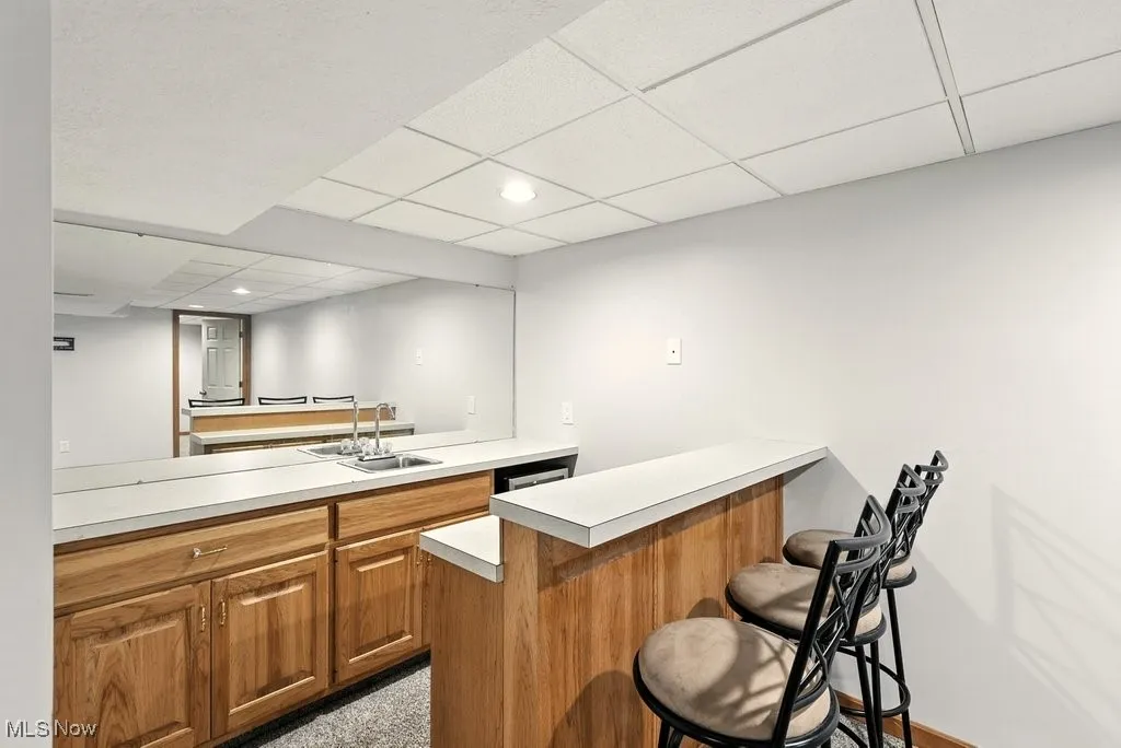 Bar featuring a drop ceiling, brown cabinets, light countertops, and recessed lighting