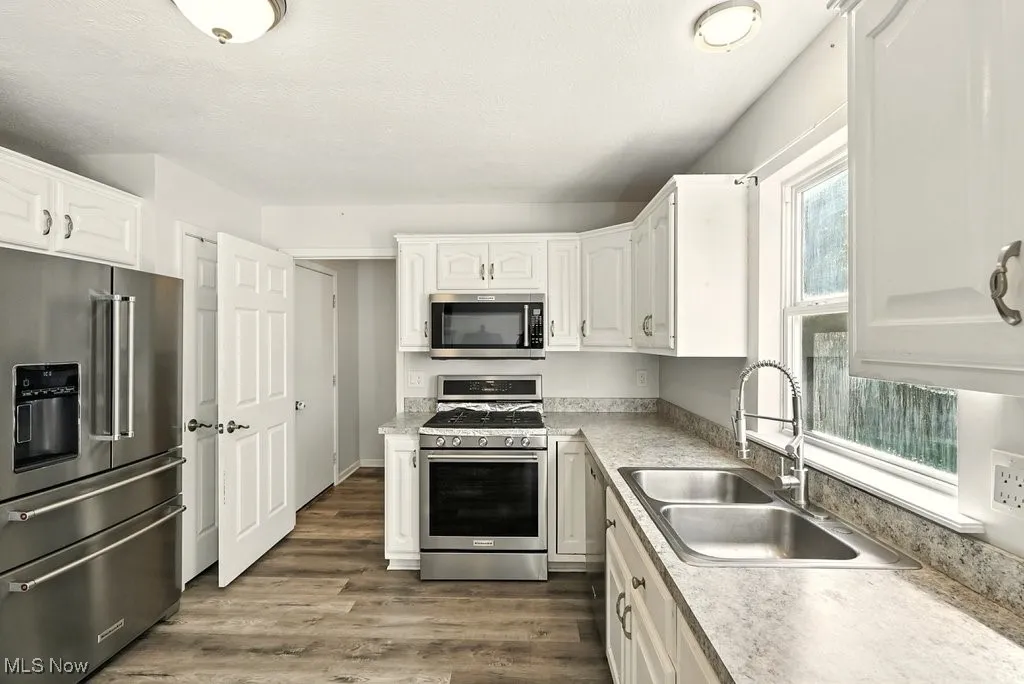 Kitchen with appliances with stainless steel finishes, dark wood-style flooring, white cabinets, and light countertops