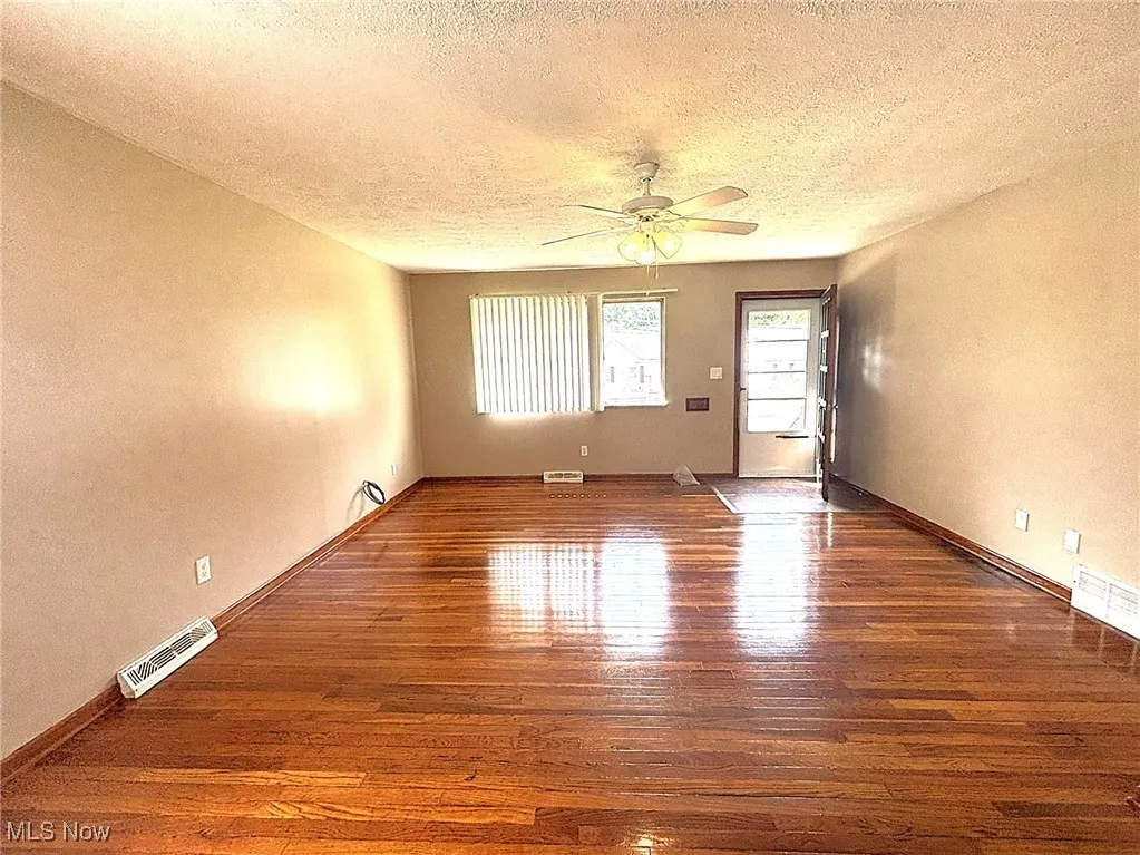 Empty room featuring hardwood / wood-style floors, a textured ceiling, a ceiling fan, and a textured wall