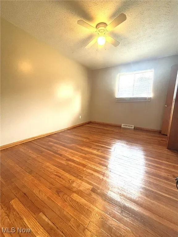 Empty room with a textured ceiling, light wood finished floors, and ceiling fan