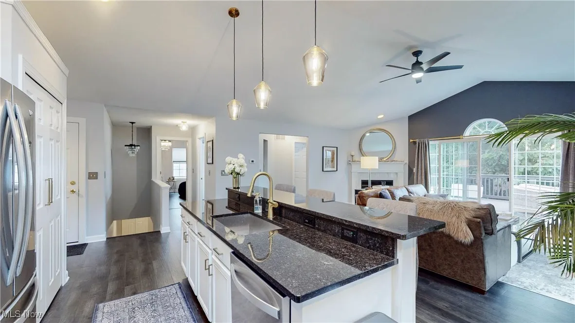 Kitchen featuring white cabinetry, stainless steel appliances, hanging light fixtures, dark wood-style floors, and dark stone counters