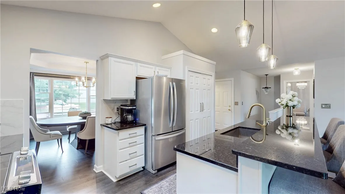 Kitchen featuring white cabinets, hanging light fixtures, a center island with sink, freestanding refrigerator, and dark wood-style​​‌​​​​‌​​‌‌​‌‌​​​‌‌​‌​‌​‌​​​‌​​ flooring