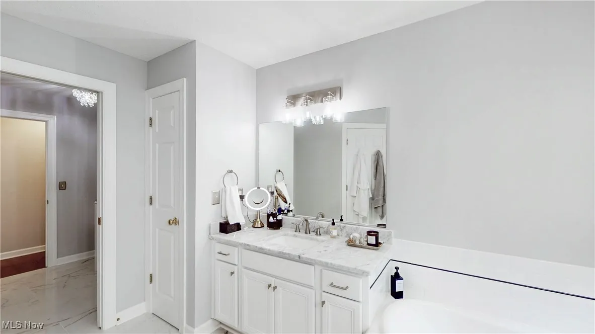 Bathroom featuring vanity, light marble finish flooring, and a garden tub