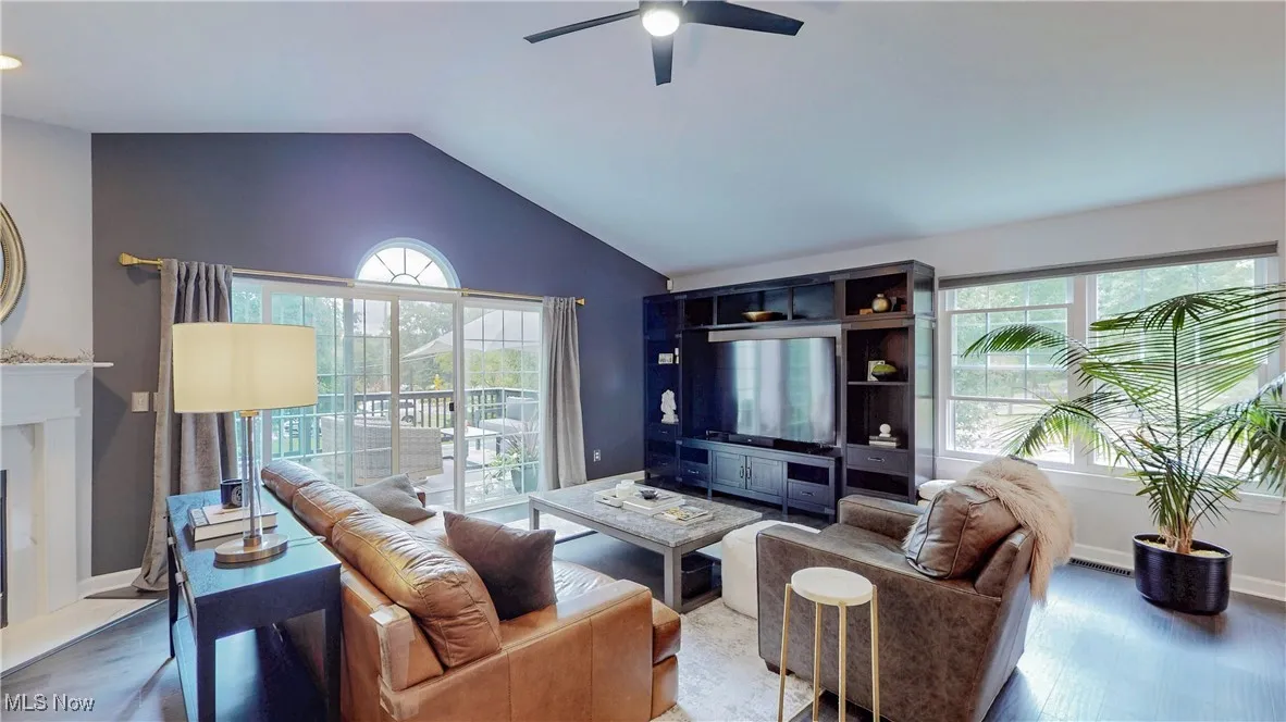 Living area featuring healthy amount of natural light, wood finished floors, lofted ceiling, a premium fireplace, and a ceiling fan