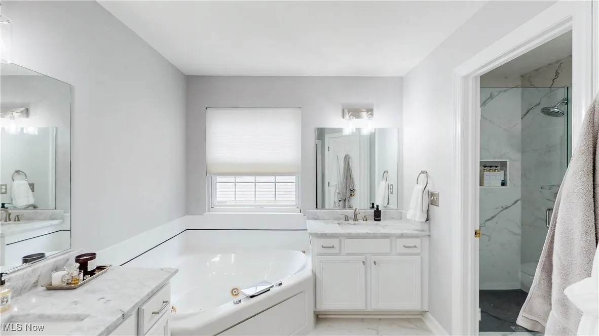 Full bathroom with a whirlpool tub, two vanities, a marble finish shower, and light marble finish flooring