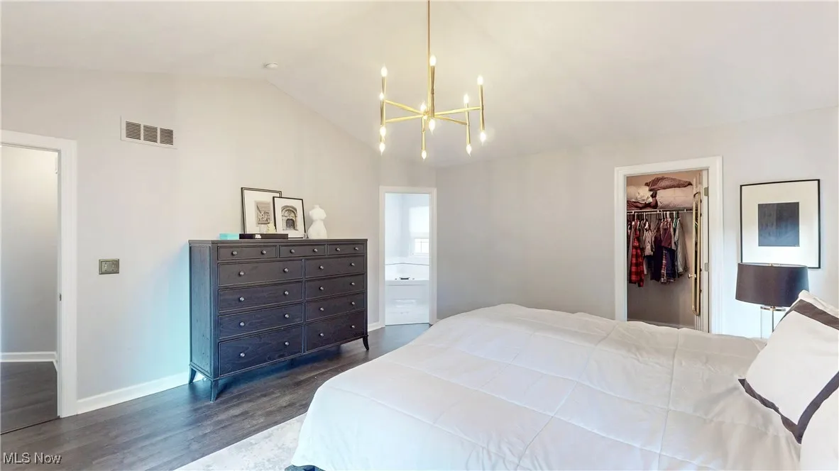 Bedroom with lofted ceiling, a chandelier, a walk in closet, dark wood-style flooring, and connected bathroom