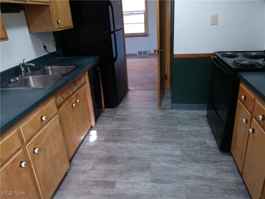 Kitchen with dark countertops, black appliances, brown cabinetry, and dark wood-type flooring