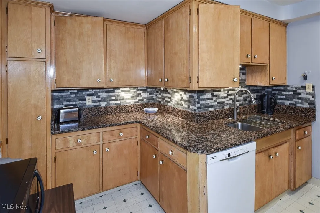 Kitchen with tasteful backsplash, dishwasher, dark stone countertops, brown cabinets, and light flooring