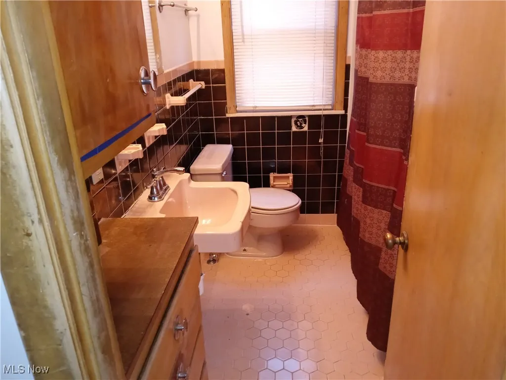 Bathroom with tile walls, tile patterned floors, vanity, and a shower with shower curtain