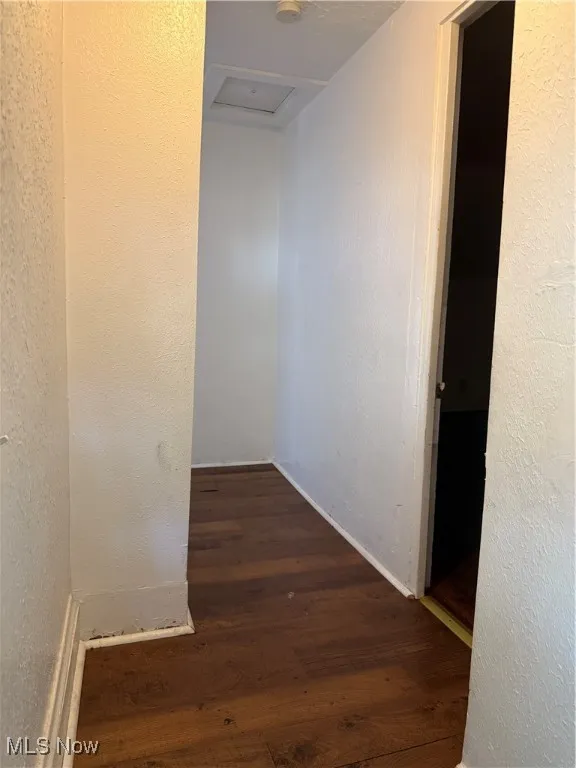 Hall featuring a textured wall, dark wood-style floors, and attic access