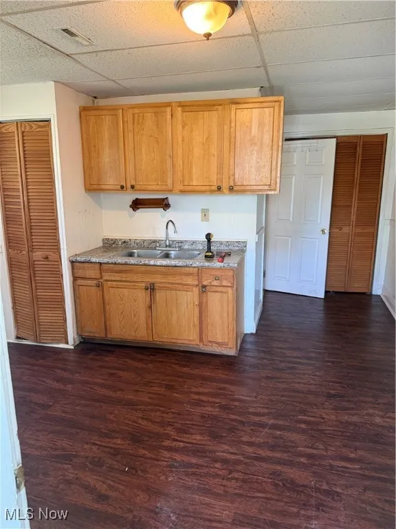 Kitchen with dark wood-type flooring, a paneled ceiling, light countertops, and brown cabinets
