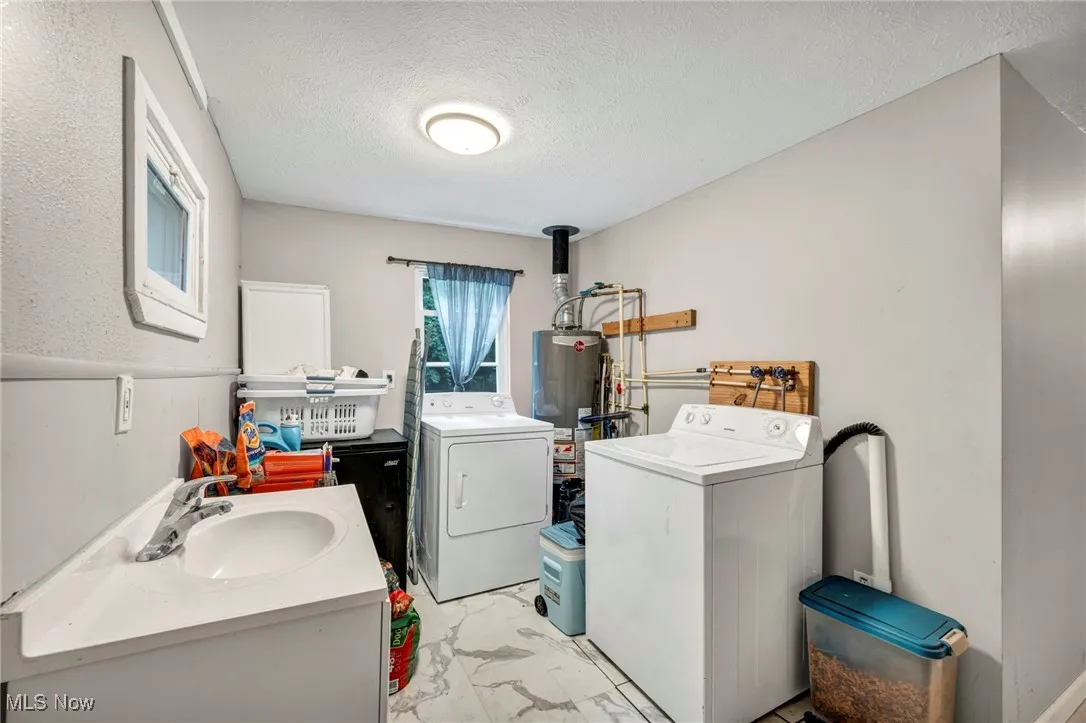 Laundry room with light marble finish floors, a textured ceiling, washer and clothes dryer, and water heater
