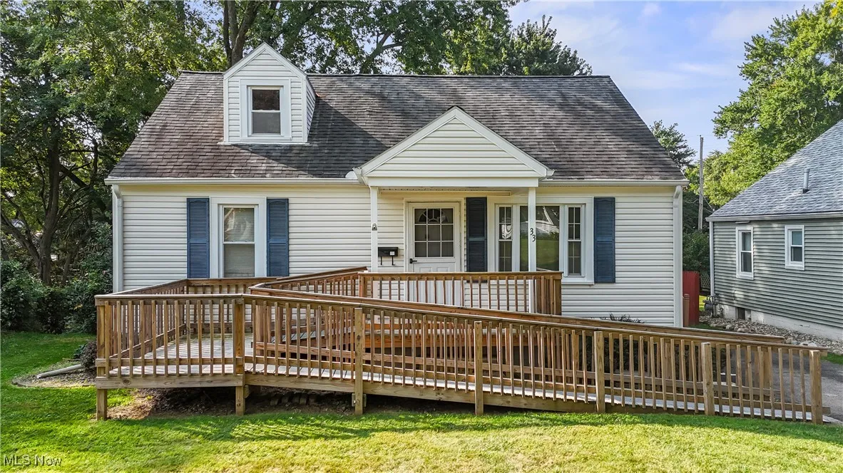 Cape cod house featuring a deck, a shingled roof, and a front yard