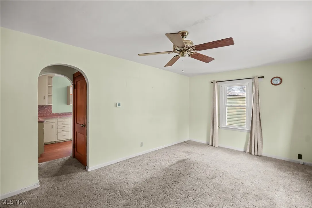 Empty room featuring arched walkways, light carpet, and ceiling fan
